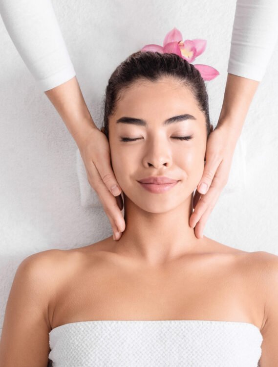 Beautiful asian woman enjoying face lifting massage, lying with closed eyes in spa salon, attractive young korean lady getting wellness treatment with professional masseur, top view with copy space